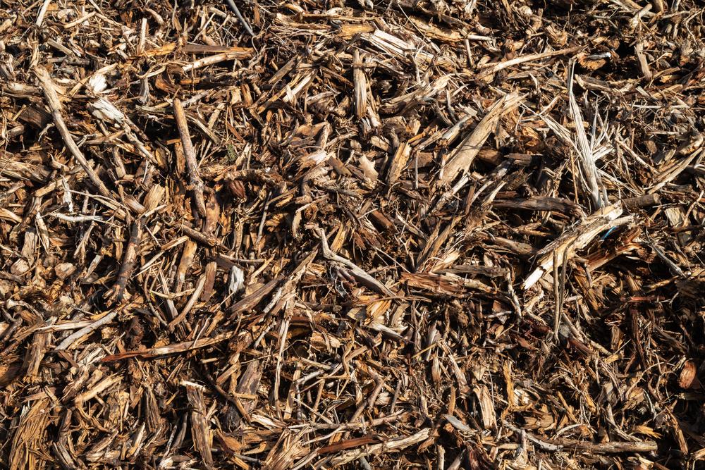 A close-up view of a pile of dry wood chips and mulch, showing rough, uneven pieces in various shades of brown.